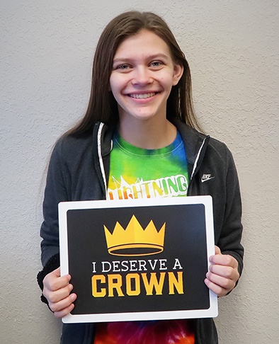 Young girl holding a sign that says I deserve a crown after orthodontic treatment
