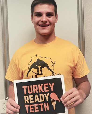 Teen with a sign reading turkey ready teeth after completing orthodontic treatment at Thanksgiving time