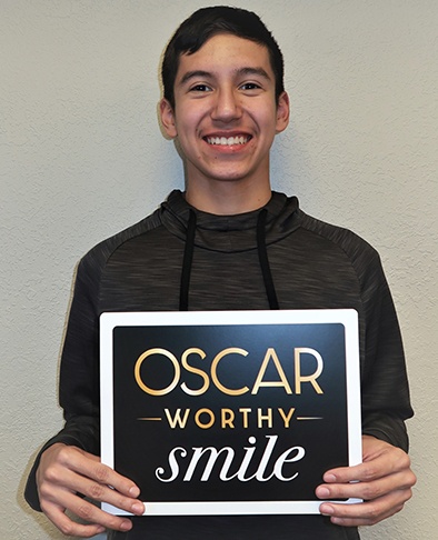 Teem boy holding up sign reading Oscar worthy smile after completing his orthodontic treatment