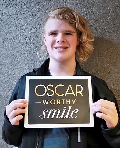 Teen holding ups sign reading Oscar worthy smile celebrating end of orthodontic treatment