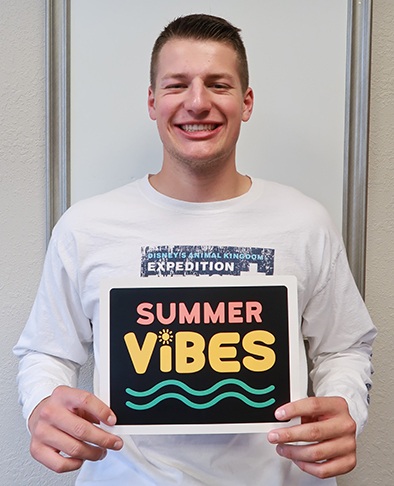 Young man holding up sign reading summer vibes after finishing his orthodontic treatment