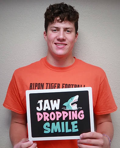 Young man holding sign with shark reading Jaw dropping smile after orthodontic treatment