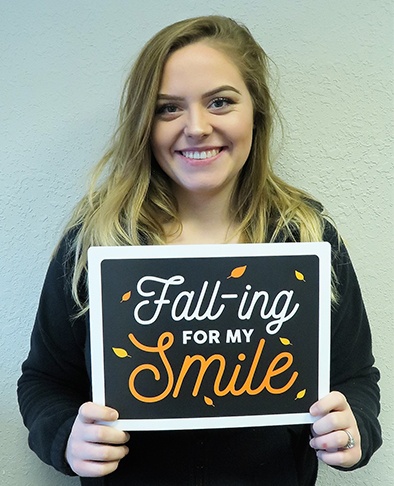 Young woman holding sign reading Falling for my smile after orthodontic treatment