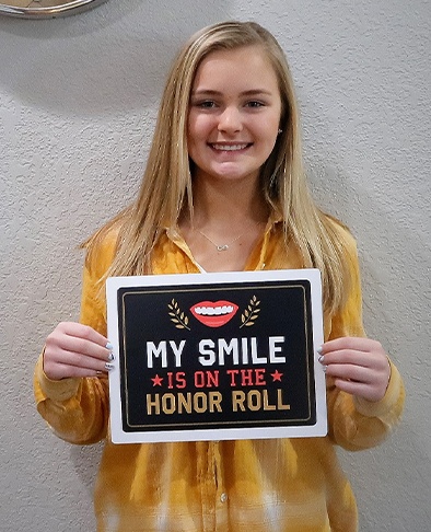 Young woman holding sign reading my smile is on the honor roll after orthodontic treatment